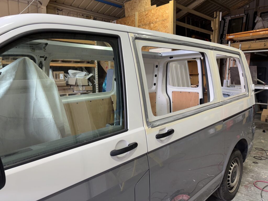 Van side windows cut out and masked ready for glazing during a camper conversion