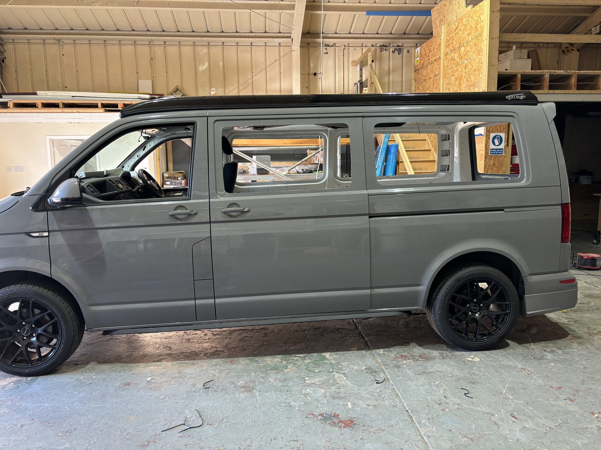 Grey VW Transporter mid-conversion in the workshop with windows cut out and pop-top roof fitted